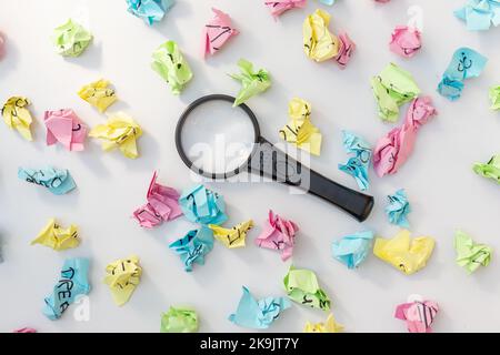 Searching for idea with a magnifying glass searching tool in crumbled paper balls Stock Photo