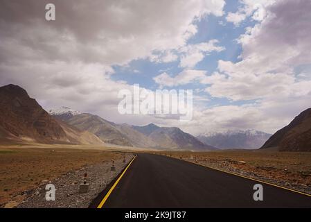 A tarmac road stretches across a wide open plain in the high altitude area of Ladakh Zanskar of North Indian HImalayas Stock Photo