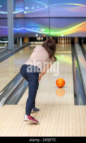 A woman throws a ball into a bowling alley. Paths with balls and pins for bowling. A fun game for the company. Stock Photo