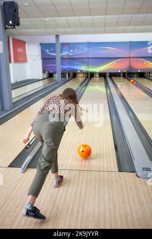 A woman throws a ball into a bowling alley. Paths with balls and pins for bowling. A fun game for the company. Stock Photo