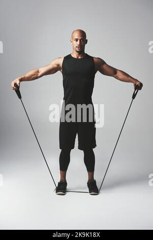 Pulling his weight. Studio portrait of an athletic young man working out with a resistance band against a grey background. Stock Photo