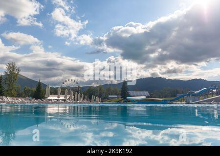 A large swimming pool with clear water in the open air against the backdrop of beautiful nature. A swimming pool with slides, sun loungers on site, a Stock Photo