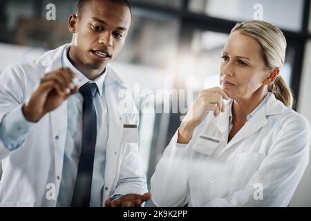 Its all in the formula. two scientists writing down formulas on a glass wipe board while doing research in their lab. Stock Photo