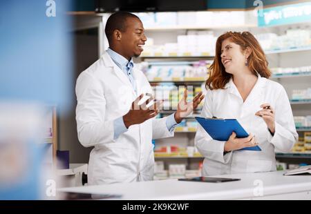 Discussing all that needs to get done for the day. two pharmacists working together in a chemist. Stock Photo