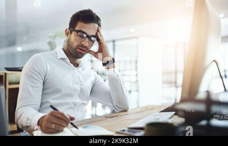 How much longer till this boring day ends. a young businessman looking bored while working in an office. Stock Photo