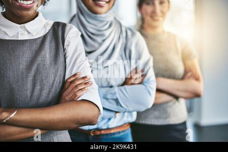 They are confident but also serious. a group of confident young businesswomen standing with their arms folded inside of the office at work. Stock Photo