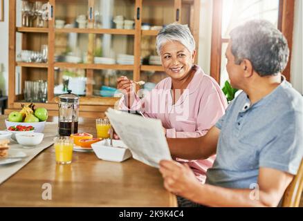 They look at each other the same way they always have. a carefree elderly couple having breakfast together while reading the paper and browsing on a Stock Photo
