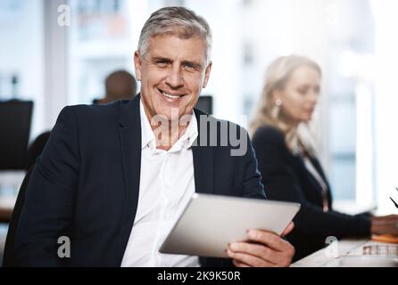 Its my go-to device for business tasks. Portrait of a mature businessman using a digital tablet in an office. Stock Photo