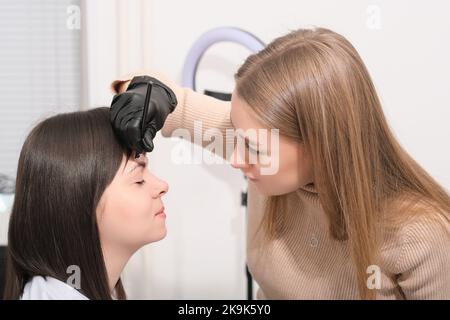 woman beautician making marks on client's face for brow mapping in salon. brow correction procedure. Permanent make-up for eyebrows. Stock Photo