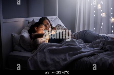 Snuggling up with a good story on their device. a mother and her little daughter using a digital tablet together in bed at night. Stock Photo