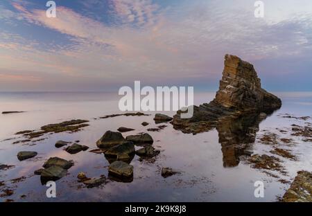 Colorful sunset over the Black Sea coast of Bulgaria with a sea stack and rocks in the calm water Stock Photo