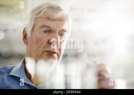 Every great business started out as an idea. a senior businessman writing down ideas with a pen marker on a glass wall in the office. Stock Photo