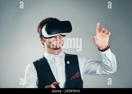Opening up a world of possibilities. Studio shot of a handsome young businessman using a vr headset against a grey background. Stock Photo
