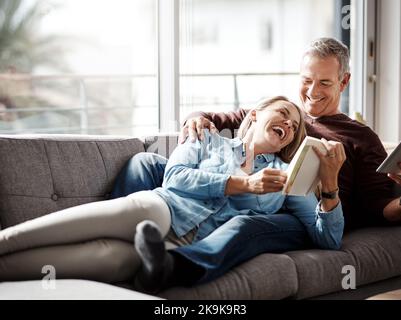 Share the love, share the laughter. a mature couple reading a book together while relaxing on the sofa at home. Stock Photo