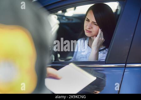 Another fine. an unrecognizable male traffic officer issuing a ticket to a female civilian at a roadblock. Stock Photo