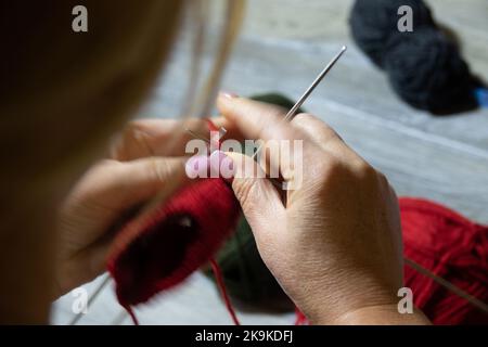 Woman hands knitting sock with needles and yarn of red color. Closeup of the hands. Blurred hand movement Stock Photo