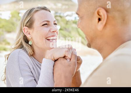 Beach, holding hands and man propose to woman on holiday by sea, happy and smiling together. Affection, romance and multicultural couple by ocean Stock Photo