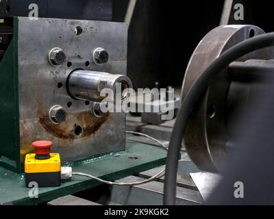 Large steel square with a mechanical coupling part in the center. A slightly blurred emergency stop button in foreground. Stock Photo