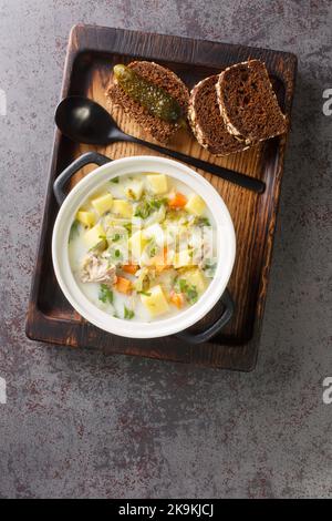 Polish creamy soup with pickled cucumbers, meat and vegetables close-up in a saucepan on a wooden board. Vertical top view from above Stock Photo