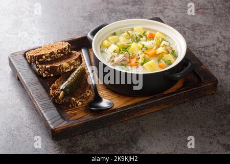 Ogorkowa Polish Sour Pickle Soup closeup on the pot on the wooden tray. Horizontal Stock Photo