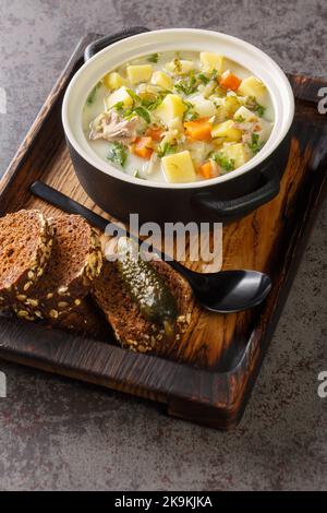 Polish creamy soup with pickled cucumbers, meat and vegetables close-up in a saucepan on a wooden board. Vertical Stock Photo