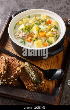 Creamy Pickle Soup Zupa Ogorkowa closeup on the pot on the wooden tray. Vertical Stock Photo