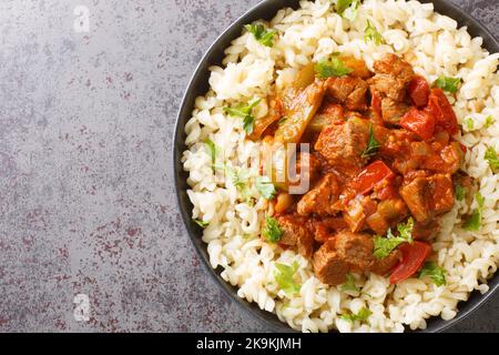 Porkolt is a Hungarian stew with boneless meat, paprika and some vegetables served with Egg Noodles Nokedli closeup on the plate on the table. Horizon Stock Photo