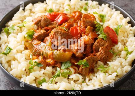 Porkolt is a Hungarian stew with boneless meat, paprika and some vegetables served with Egg Noodles Nokedli closeup on the plate on the table. Horizon Stock Photo
