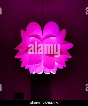 Floral shaped chandelier glowing with hot pink light isolated on dark background Stock Photo