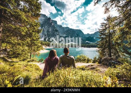Description: Young couple enjoys beautiful view on Baires Lake in the Dolomite mountains in the afternoon. Braies Lake (Pragser Wildsee, Lago di Braie Stock Photo