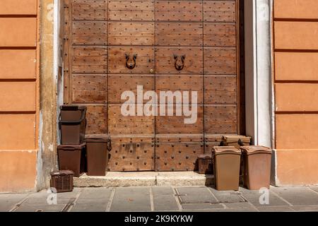 Bins with biological waste on the sidewalk in front of a historic door in the village of Foligno in the central Italian regio Umbria. Stock Photo