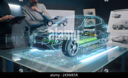 Car design engineers using holographic app in digital tablet. Develop modern innovative high-tech cutting edge eco-friendly electric car with sustainable standards. They test the aerodynamic qualities Stock Photo