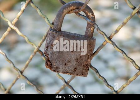 Old weathered rusty padlock locked on iron fence grid closeup Stock Photo
