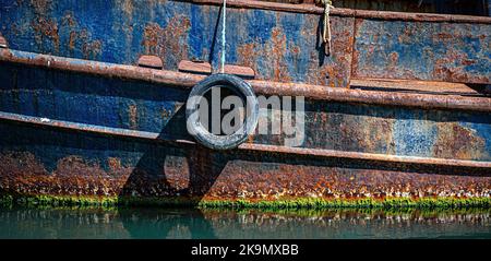 Tyre hanging on the side of a rusty fishing boat to protect it from knocks. Stock Photo