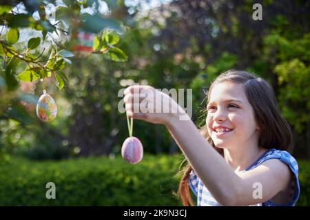 Girl Hanging Homemade Easter Decorations Outdoors On Tree In Garden At Home Stock Photo