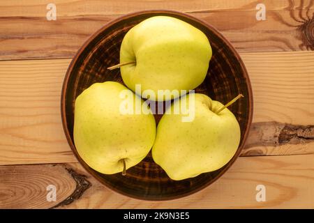 Three ripe yellow apples with a clay plate on a wooden table, macro, top view. Stock Photo