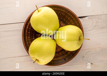 Three ripe yellow apples with a clay plate on a wooden table, macro, top view. Stock Photo