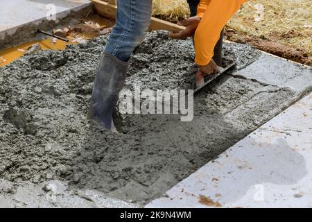 Mason worker is holding steel trowel and smoothing plastering new sidewalk on wet freshly poured concrete in construction site Stock Photo
