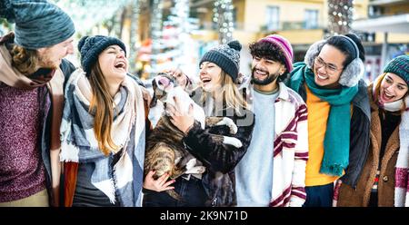 Happy friends group having fun together with cute dog on winter holidays - Life style concept with trendy young people wearing fashion clothes outdoor Stock Photo