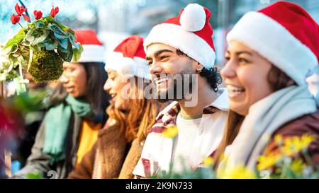 Happy friends having fun shopping at Christmas market on winter time - Urban holiday concept with young people hanging out together wearing santa hat Stock Photo