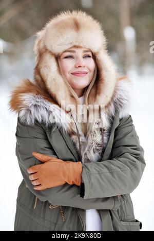 Portrait of young woman in warm clothes wearing winter parka jacket with fur, fur hat, leather gloves. Cold weather clothing