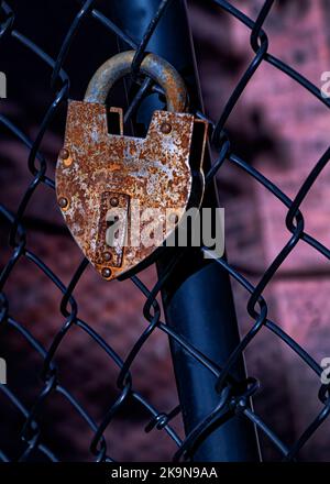 Heart-shaped rusty padlock on a black chain-link fence . Stock Photo