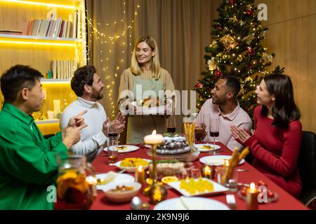 multiethnic group of happy friends having christmas dinner together at home together. holidays and celebration concept. thanksgiving day The hostess will serve the turkey. reunion party Stock Photo