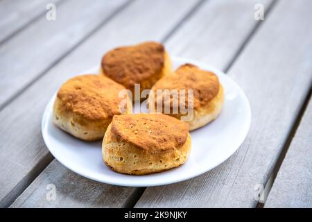 Macro closeup on four cooked homemade buttermilk breakfast biscuits on white plate at kitchen wooden table Stock Photo