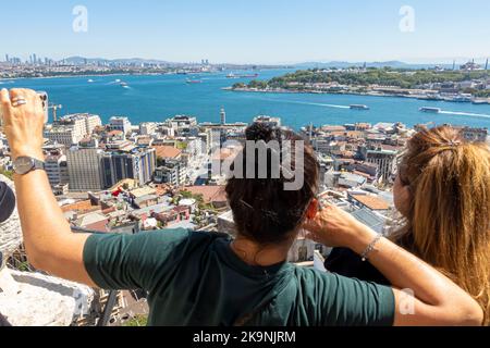Couple, man and woman taking selfie in Galata Tower with view of the city of Istanbul and Bosphor. Tourists doing selfie. Stock Photo