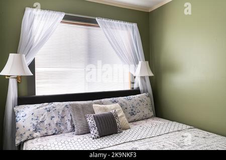 Bedroom room with lamps lights, pillows with sheet on mattress bed headboard in modern hotel motel room with white curtains and green painted walls Stock Photo