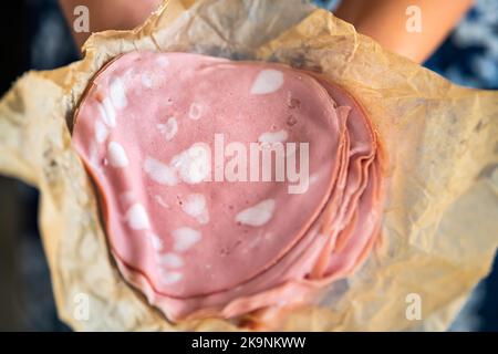 Macro closeup of thin slices, sliced cut pork cured Italian mortadella sausage soft bologna with fat and sandwich pink meat in paper package wrap Stock Photo