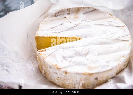 French soft brie cheese round wheel in paper package, dairy double cream product on kitchen table macro closeup with cut slice Stock Photo