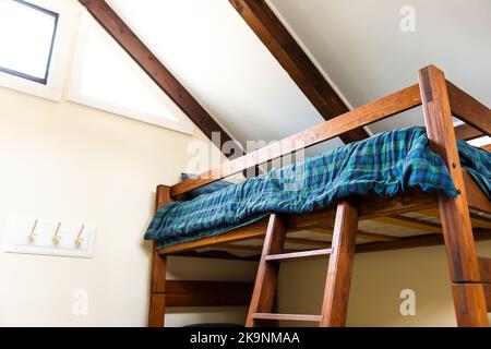 Wooden bunk bed with wood ladder and retro vintage comforter blanket in vaulted attic roof lodge cabin room with bright natural light