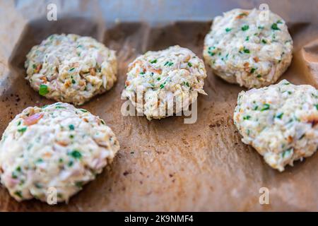 Macro closeup of raw uncooked crab crabmeat fish cakes on parchment paper of baking oven tray in kitchen with herns Stock Photo